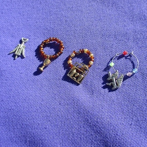 May include: Five different wine glass charms, each with a different design. The charms are made of metal and have a variety of colors, including silver, gold, and red. The charms are attached to a ring that can be placed on a wine glass.