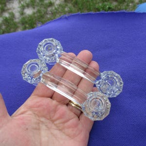 May include: Two clear glass drawer pulls featuring a curved handle design and faceted, octagonal mounting bases. Each handle has a smooth, transparent center section and textured, geometric ends that provide a decorative appearance for furniture.