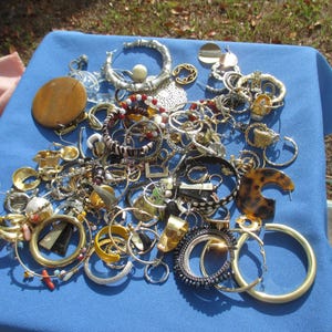 May include: A collection of assorted jewelry, including rings, bracelets, and earrings, displayed on a blue cloth. The jewelry features various designs, colors, and materials, including gold, silver, and tortoiseshell patterns. Some pieces have beads and gemstones.