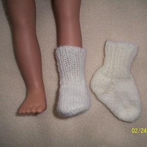May include: A pair of white knitted socks. One sock is on a doll's foot, and the other sock is lying flat on a white surface. The date 02/24/2010 is written in the bottom right corner of the image.