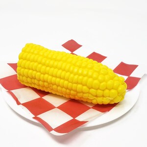 Puede incluir: Una mazorca de ma&iacute;z amarilla sobre una servilleta de papel a cuadros rojos y blancos.