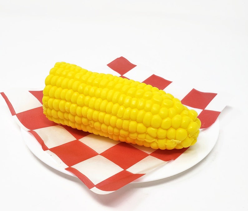 Puede incluir: Una mazorca de ma&iacute;z amarilla sobre una servilleta de papel a cuadros rojos y blancos.