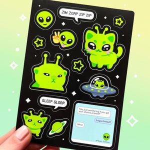 May include: Black sticker sheet with green alien designs, including a cat-like alien, a UFO, and speech bubbles with text. The text includes phrases like "Zim Zorp Zip Zip" and "Gleep Glorp."