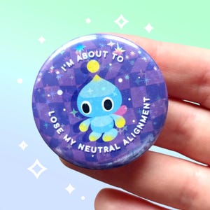 May include: A round button with a purple background and the text "I'M ABOUT TO LOSE MY NEUTRAL ALIGNMENT". The button features a blue cartoon character with yellow accents and a pink wing.