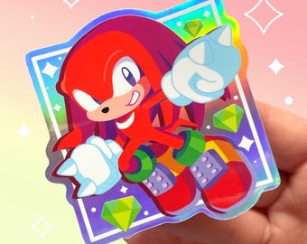 May include: A holographic sticker featuring Knuckles the Echidna from the Sonic the Hedgehog video game series. Knuckles is depicted in a red and yellow outfit, with a determined expression and his signature spiked knuckles. The sticker is surrounded by a rainbow-colored border and features green gems scattered around Knuckles.