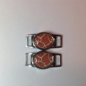 May include: Two silver shoe charms with a brown and white giraffe print design.