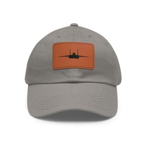 May include: A gray baseball cap with a brown leather patch featuring a silhouette of a fighter jet.