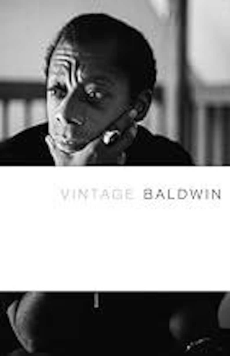 May include: Black and white photograph of James Baldwin, with the text "VINTAGE BALDWIN" in a minimalist font. Baldwin is shown with his hand on his chin, looking thoughtful. The image is a portrait, likely for a book cover or print.