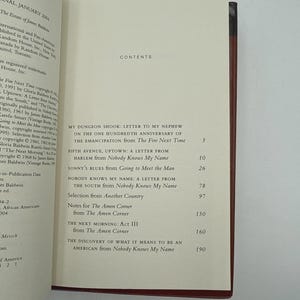 May include: Open book with a red spine, displaying the contents page of a book. The title "Nobody Knows My Name" is visible, along with other chapter titles. The book is open to a page with text.