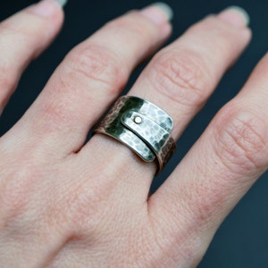 K&ouml;nnte beinhalten: Ein silberner, geh&auml;mmerter Metallring mit einem goldenen Akzent. Der Ring wird an einem Finger getragen.