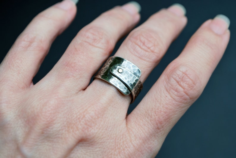 K&ouml;nnte beinhalten: Ein silberner, geh&auml;mmerter Metallring mit einem goldenen Akzent. Der Ring wird an einem Finger getragen.