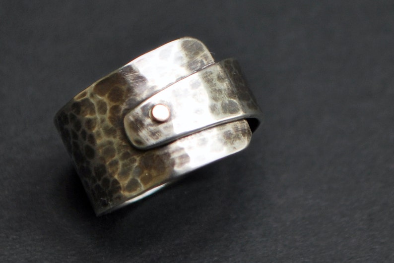 K&ouml;nnte beinhalten: Ein silberner Ring mit geh&auml;mmerter Textur und einem kleinen, runden Akzent aus Ros&eacute;gold. Der Ring ist so konzipiert, dass er am Finger getragen wird, wobei die geh&auml;mmerte Seite nach au&szlig;en zeigt.