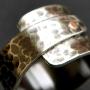 K&ouml;nnte beinhalten: Ein silberner Ring mit geh&auml;mmerter Textur und einem kleinen goldenen Akzent. Der Ring besteht aus zwei B&auml;ndern, die umeinander gewickelt sind.