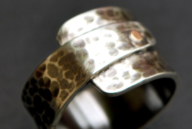 K&ouml;nnte beinhalten: Ein silberner Ring mit geh&auml;mmerter Textur und einem kleinen goldenen Akzent. Der Ring besteht aus zwei B&auml;ndern, die umeinander gewickelt sind.