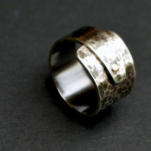 K&ouml;nnte beinhalten: Ein silberner Ring mit geh&auml;mmerter Textur und einem goldenen Akzent. Der Ring ist so konzipiert, dass er am Finger getragen wird, wobei der goldene Akzent nach au&szlig;en zeigt.