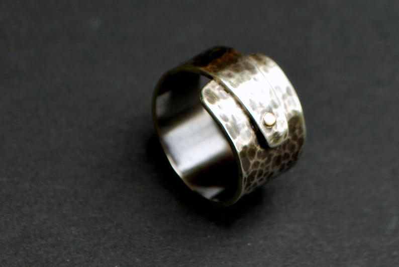 K&ouml;nnte beinhalten: Ein silberner Ring mit geh&auml;mmerter Textur und einem goldenen Akzent. Der Ring ist so konzipiert, dass er am Finger getragen wird, wobei der goldene Akzent nach au&szlig;en zeigt.
