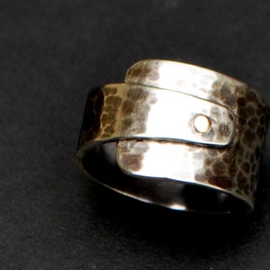 K&ouml;nnte beinhalten: Ein silberner Ring mit geh&auml;mmerter Textur und einem goldenen Akzent. Der Ring ist breit und hat ein einzigartiges Design.