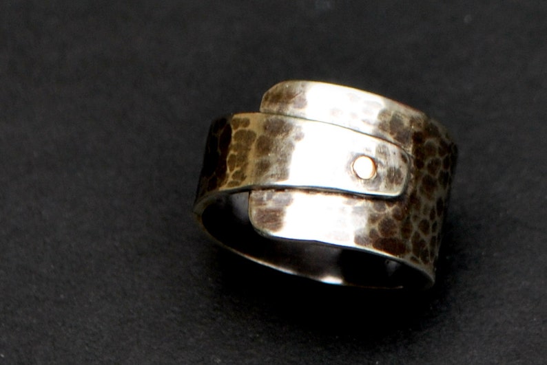 K&ouml;nnte beinhalten: Ein silberner Ring mit geh&auml;mmerter Textur und einem goldenen Akzent. Der Ring ist breit und hat ein einzigartiges Design.