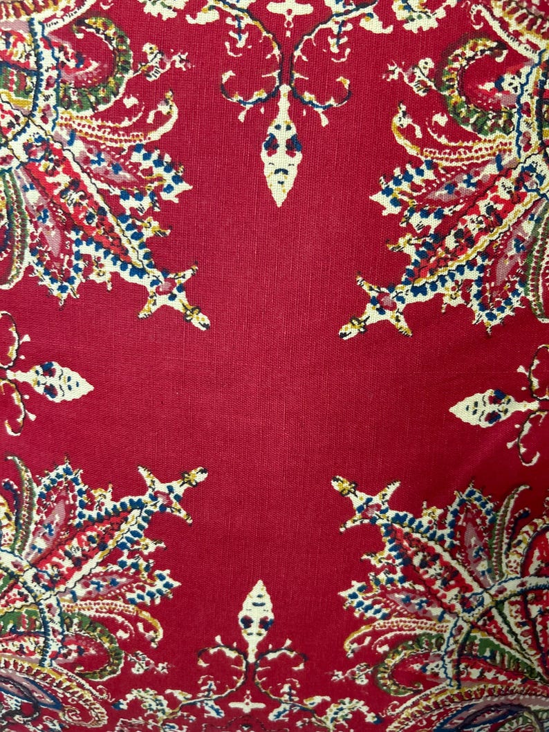 May include: Red fabric with a paisley pattern. The fabric has a textured surface and is decorated with a repeating pattern of intricate floral designs in shades of blue, green, and white.