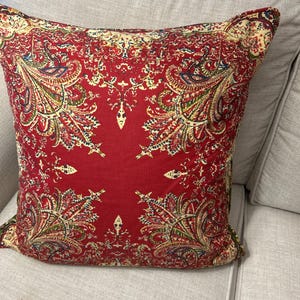 May include: Red cushion with a paisley pattern in shades of yellow, green, and blue.