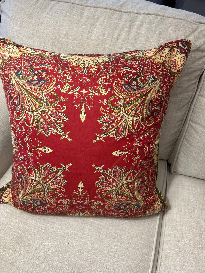 May include: Red cushion with a paisley pattern in shades of yellow, green, and blue.