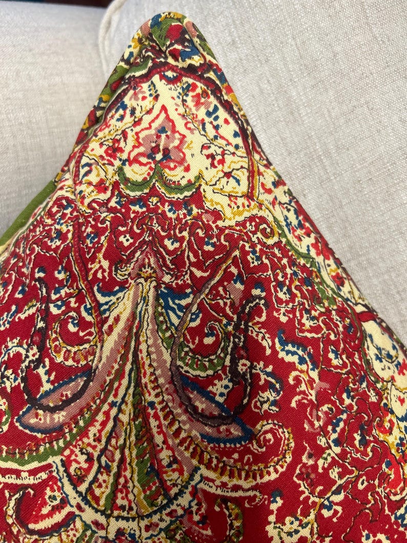 May include: Red, green and blue paisley patterned throw pillow with a cream background.