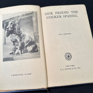 May include: A black and white photo of a Cocker Spaniel dog sitting on a white background. The book cover reads "Our Friend the Cocker Spaniel" with a frontispiece. The book is published by E.P. Dutton & Co., Inc. in New York.