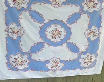 May include: A white tablecloth with a light blue border and floral pattern. The border has a scalloped design with red accents. The floral pattern includes red, white, and blue flowers.