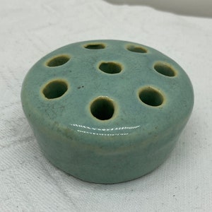 May include: A light blue ceramic flower frog with seven holes for arranging flowers.