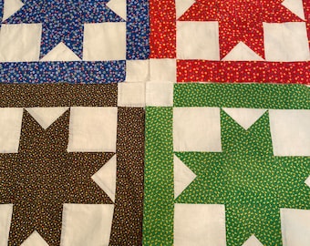 May include: A patchwork quilt with four squares, each featuring a white star on a different colored background. The squares are blue, red, brown, and green. Each square has a small floral pattern.
