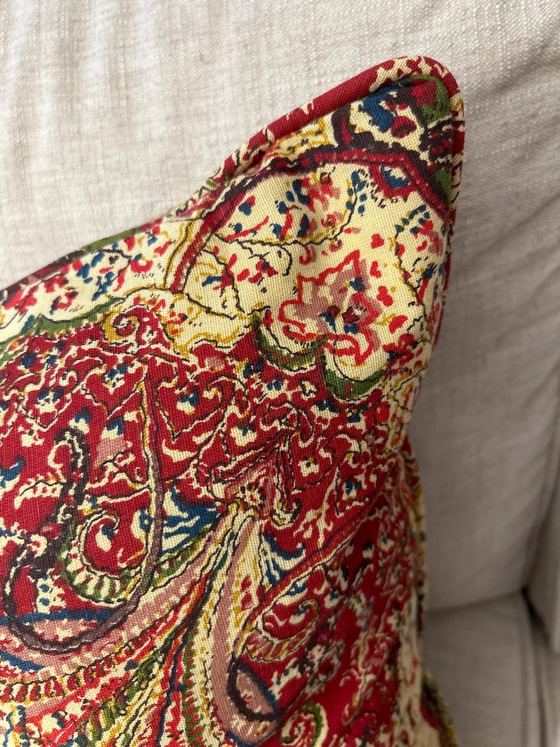 May include: A red, yellow, blue and green paisley patterned throw pillow with a cream background.