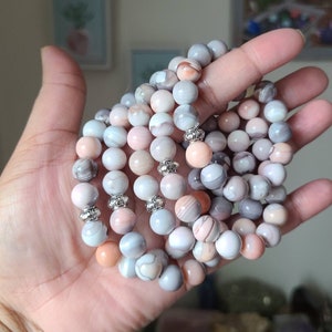Op de afbeelding: Een stapel armbanden gemaakt van roze en grijze agaat kralen met zilveren accenten.
