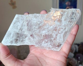 May include: A large, clear selenite crystal slab with a rough, textured surface. The crystal is translucent and has a slight shimmer.