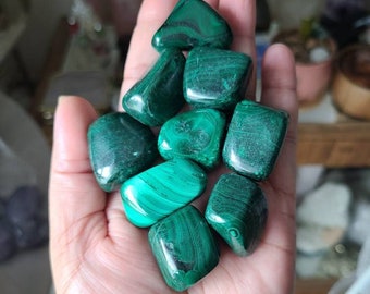 May include: A collection of eight green malachite tumbled stones, each with a unique pattern of swirling green veins. The stones are approximately 1 inch in size and are arranged in a hand.