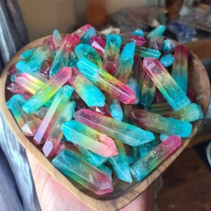 May include: A bowl filled with colorful, iridescent crystal points. The points are in shades of blue, green, pink, and yellow. The bowl is made of wood and has a heart shape.
