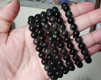 May include: A stack of black obsidian bracelets with iridescent shimmer. Each bracelet is made of round beads.