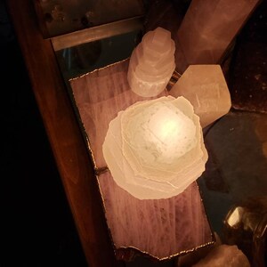 Op de afbeelding: Een witte selenietkristal lamp op een houten dienblad met een roze en witte agaatbasis. De lamp is aan en gloeit.