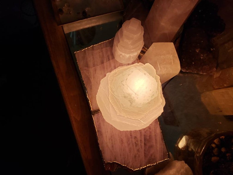 Op de afbeelding: Een witte selenietkristal lamp op een houten dienblad met een roze en witte agaatbasis. De lamp is aan en gloeit.