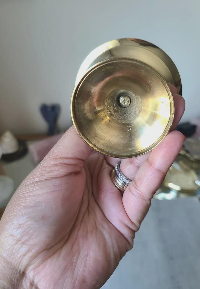 Pu&ograve; includere: Un portacandele vintage in ottone con una base ampia e circolare e una parte superiore leggermente svasata. L'ottone ha una calda tonalit&agrave; dorata e la base mostra segni di et&agrave; e utilizzo. Il portacandele &egrave; progettato per contenere una singola candela.