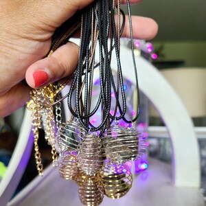 May include: A collection of necklaces with caged crystal pendants. The pendants are made of gold wire and contain various types of crystals, including amethyst, rose quartz, and black obsidian. The necklaces are strung on black and brown cords.