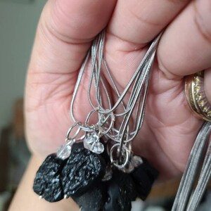 May include: A set of silver chain necklaces with black obsidian stone pendants. Each pendant is a rough, irregular shape and has a small clear crystal charm attached.