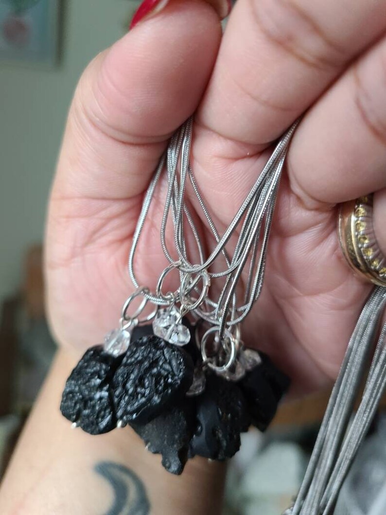May include: A set of silver chain necklaces with black obsidian stone pendants. Each pendant is a rough, irregular shape and has a small clear crystal charm attached.