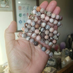 Op de afbeelding: Een stapel armbanden gemaakt met agaat kralen in tinten bruin, roze en wit. De kralen hebben een gestreept patroon en zijn versierd met goudkleurige spacers.