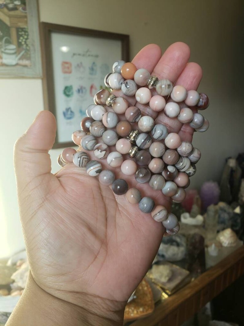 Op de afbeelding: Een stapel armbanden gemaakt met agaat kralen in tinten bruin, roze en wit. De kralen hebben een gestreept patroon en zijn versierd met goudkleurige spacers.