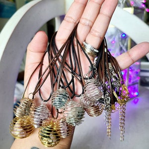 May include: A collection of necklaces with caged crystal pendants. The pendants are made of silver and gold wire and contain various types of crystals. The necklaces are made of brown cord.