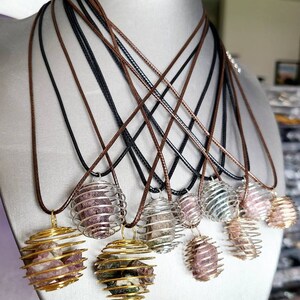 May include: A set of eight necklaces with crystal cage pendants. Each pendant features a different colored crystal encased in a gold or silver wire cage. The necklaces are displayed on a mannequin and have brown and black cords.