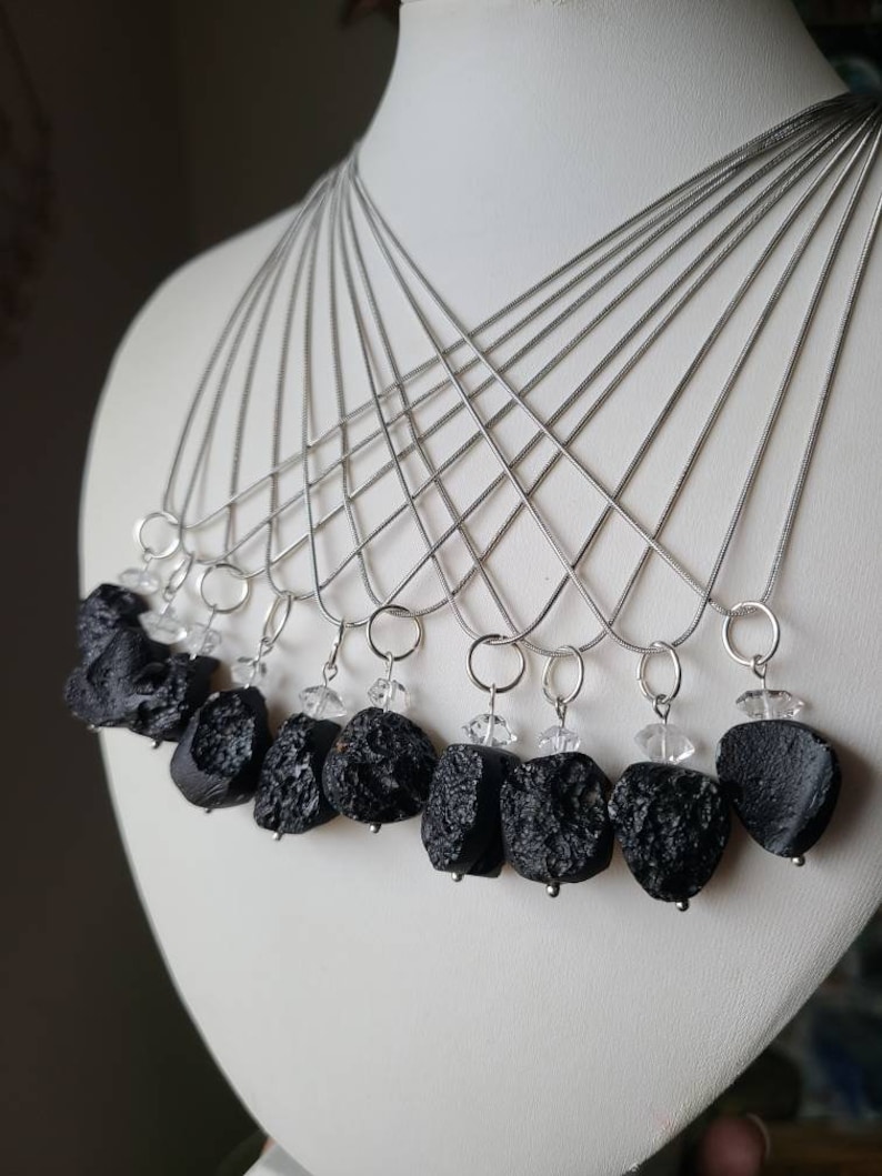 May include: A set of ten silver necklaces with black lava rock pendants and clear crystal accents.