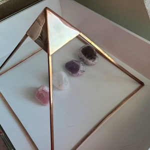 May include: A copper wire pyramid with four smooth, rounded stones inside. The stones are various shades of purple and pink.