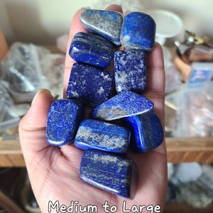 May include: A collection of ten tumbled lapis lazuli stones in various shades of blue with white and gold flecks. The stones are medium to large in size, measuring 0.9"-1.1" in diameter.