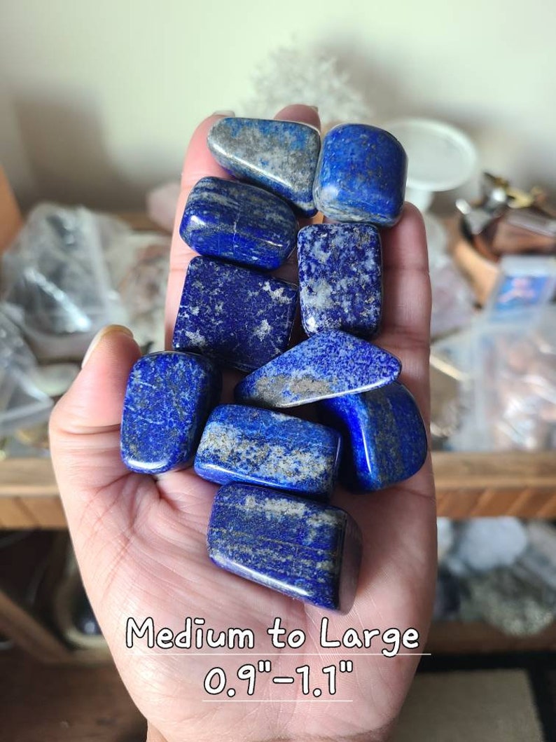 May include: A collection of ten tumbled lapis lazuli stones in various shades of blue with white and gold flecks. The stones are medium to large in size, measuring 0.9"-1.1" in diameter.